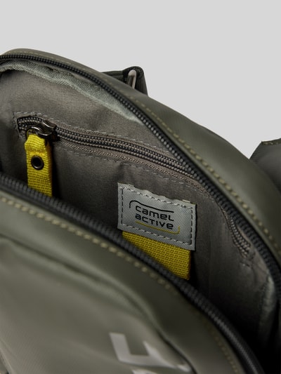 Produktfoto, Crossbody Bag mit Statement-Print Modell 'EXPLORE' von camel active in Olivgrün, Hauptfach mit Reißverschluss, Detailaufnahme, Kontext: Herren Crossbody Bag mit Reißverschlussfach, verstellbare Schulterriemen, Maße 20x22x5 cm, Schulterriemen 106 cm.