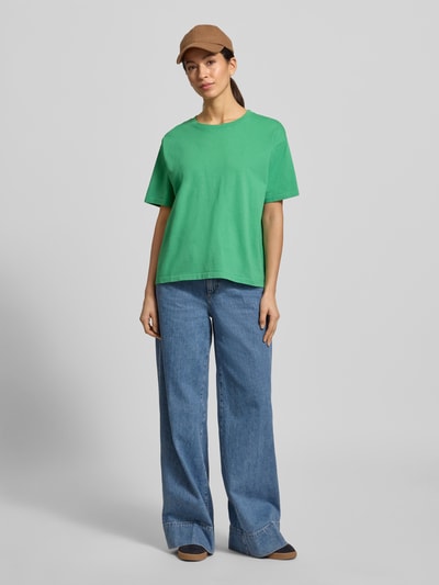 Frauenmodel trägt Loose Fit T-Shirt aus reiner Baumwolle Modell 'VALLEY' von American Vintage in Grün, Damen T-Shirt mit Rundhalsausschnitt und überschnittenen Schultern, kombiniert mit blauer Jeans, Rückenlänge bei Größe S: 56 cm, Ganzkörperansicht von vorne.
