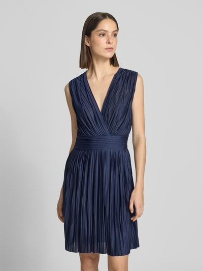 Frauenmodel trägt knielanges Cocktailkleid in Falten-Optik Modell 'Linn' von GUIDO MARIA KRETSCHMER WOMAN aus dunkelblauem Satin, taillierte Passform, tiefer V-Ausschnitt, blickdichter Unterrock, Nahaufnahme Oberkörper.
