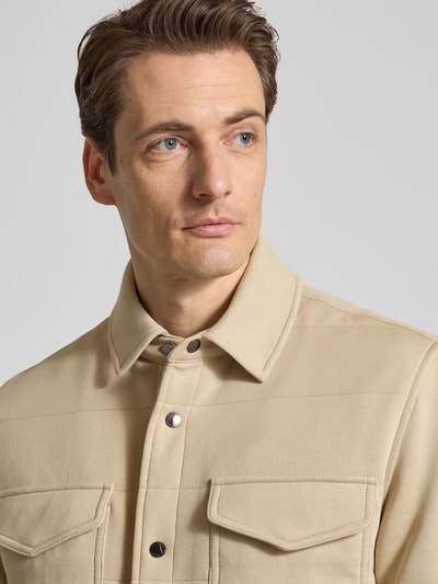 Männermodel trägt Regular Fit Sweatjacke aus Baumwoll-Mix von Tommy Hilfiger in Beige, unifarben, mit Druckknopfleiste, Nahaufnahme Oberkörper.
