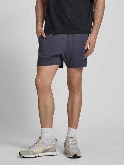 Männermodel trägt Regular Fit Shorts mit Logo-Print von PUMA PERFORMANCE in Dunkelgrau, elastischer Bund, Eingrifftaschen, Ganzkörperansicht von vorne.