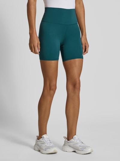 Frauenmodel trägt High Rise Radlerhose Modell 'HARMONY' von New Balance in Türkis, elastischer Bund, figurbetont, Ganzkörperansicht von vorne, Material-Mix mit Stretch-Anteil