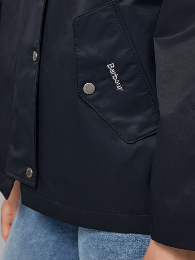 Kobieta nosi Regular Fit Parka aus Baumwoll-Mix Modell 'KINGSWOOD' od Barbour, granatowy materiał, srebrne napy, zbliżenie na kieszeń, damska parka Barbour, detal.