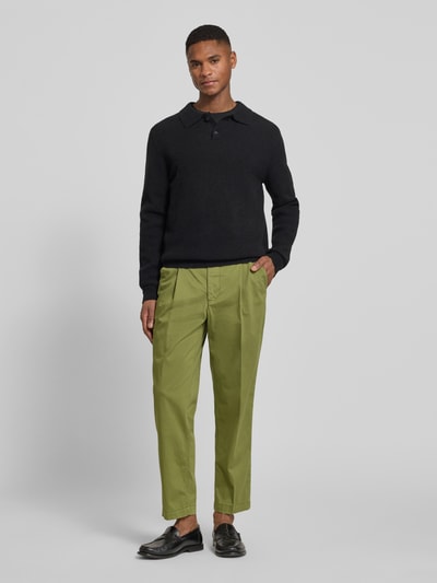 Männermodel trägt Regular Fit Chino aus Baumwoll-Mix Modell 'TAAMIR PLEATED' von Armedangels in grün, Ganzkörperansicht von vorne.