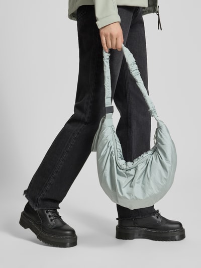 Frauenmodel trägt Umhängetasche mit verstellbarem Schulterriemen von adidas Sportswear in Unifarbe mit elastischer Raffung, Ganzkörperansicht von vorne.