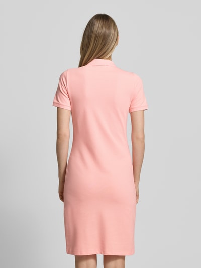 Vrouwenmodel draagt Knielanges Polokleid mit Label-Stitching van Gant in zalmroze, mix van katoen en elastaan, recht model, knielengte, labelstitching, knoopsluiting, ruglengte maat S 95 cm, borstwijdte 41 cm, mouwlengte 20 cm. Ganzkörperaanzicht achterkant.
