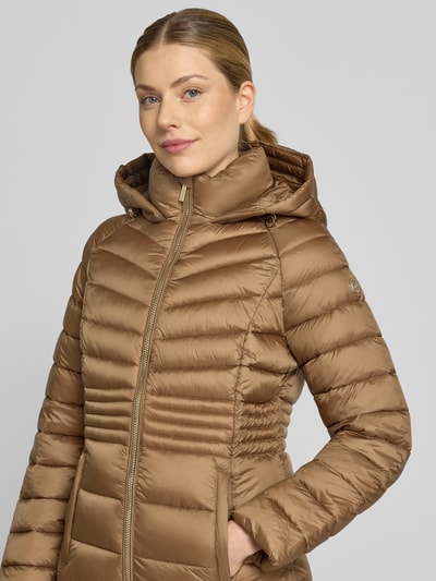 Frauenmodel trägt Steppmantel mit Reißverschlusstaschen und Kapuze von MICHAEL Michael Kors in Braun mit glänzender, gesteppter Textur, Nahaufnahme Oberkörper. Gerader Schnitt, Reißverschluss, Kapuze mit Tunnelzug, seitliche Taschen und Reißverschlüsse, S-Größe Maße.