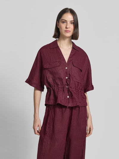 Frauenmodel trägt Relaxed Fit Leinenbluse mit Brusttaschen von Christian Berg Woman in Dunkelrot, Hemdblusenkragen, V-Ausschnitt, Brusttaschen, Knopfleiste, Schnürung, reine Leinenstruktur, Ärmel mit Aufschlag, glatte Textur, Ganzkörperansicht von vorne.