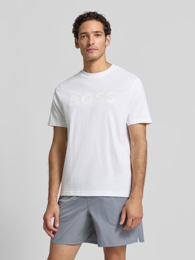 Męski model nosi białą koszulkę z logo BOSS, model 'TS_STRUCTURE LOGO 1027473' od BOSS Green, t-shirt o kroju regular fit, widok całej sylwetki z przodu.