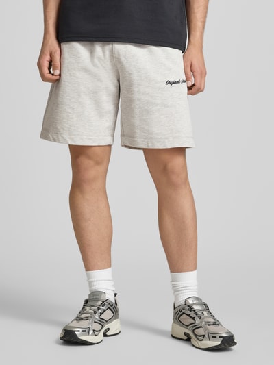 Männermodel trägt Shorts mit Label-Stitching Modell 'KARL' von Jack & Jones aus Baumwoll-Mix, Relaxed-Fit, helle Farbe, seitliche Eingrifftaschen, elastischer Bund mit Kordelzug, Ganzkörperansicht von vorne.