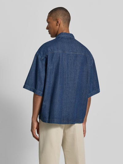 Męski model nosi Oversized Jeanshemd aus Baumwoll-Lyocell-Mix od Armedangels, niebieski denim, krój oversize, koszula z długim rękawem, detal label patch i logo-stitching, twillowa faktura, widok całej sylwetki z tyłu.