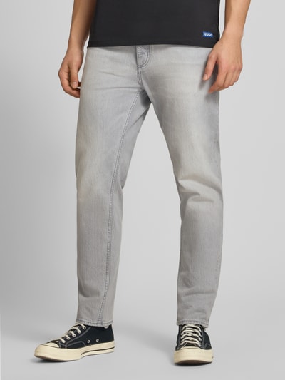 Männermodel trägt Tapered Straight Fit Jeans aus Baumwoll-Mix Modell 'BRODY' von HUGO Blue in hellgrauer Denim-Optik, Nahaufnahme Unterkörper.