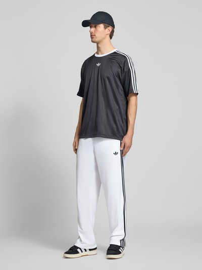 Mannelijk model draagt Regular Fit Sweatpants mit Label Print van adidas Originals, all-over motief, regular fit, labelprint, elastische boord, zij-steekzakken, voorkant geheel in beeld.