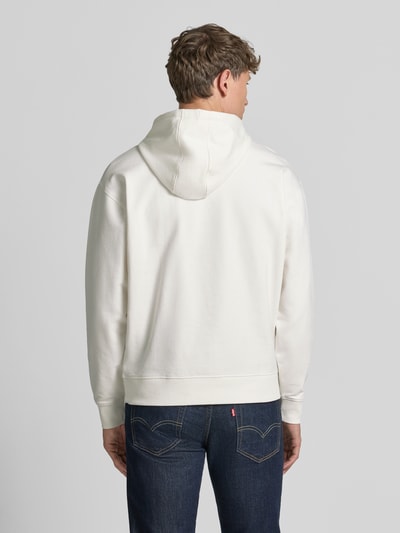 Männermodel trägt weißen Hoodie mit Label-Print und Känguru-Tasche von GUESS aus Baumwoll-Mix mit Stretch-Anteil, Ganzkörperansicht Rückansicht.