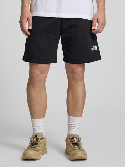 Männermodel trägt Shorts mit Logo von The North Face in Schwarz, Baumwoll-Mix, Regular-Fit, elastischer Bund, Nahaufnahme Beine, ganzkörperansicht von vorne.