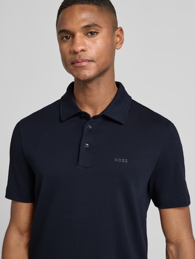 Männermodel trägt Poloshirt mit Brand-Schriftzug von BOSS in Dunkelblau, reine Baumwolle, tonaler Schriftzug, Nahaufnahme Oberkörper.