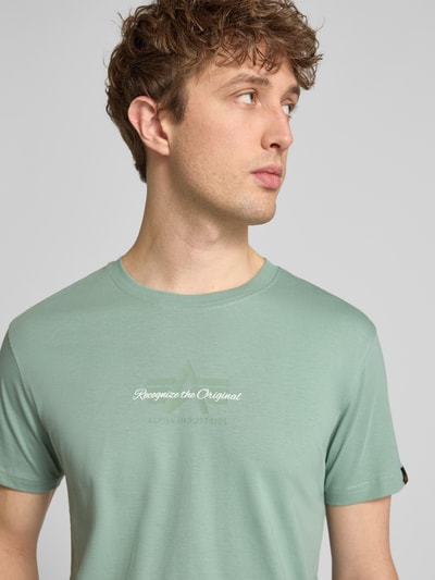 Männermodel trägt T-Shirt mit Label-Detail von Alpha Industries in Mintgrün, Reine Baumwolle, Gerader-Schnitt, Rundhalsausschnitt, Nahaufnahme Oberkörper.