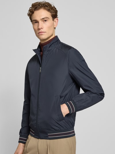 Męski model nosi Blouson mit Stehkragen und Reißverschluss od Geox, krój regular fit, granat, kieszenie, widok całej sylwetki z przodu.