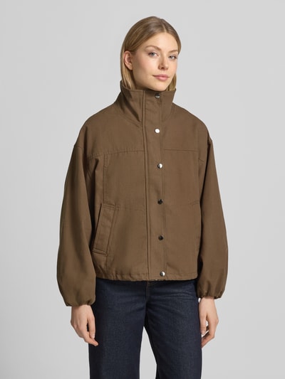 Kobieta modelka nosi bomberkę z mieszanki materiałów z dodatkiem streczu Neo Noir Bomberjacke mit Stehkragen Modell 'Selio', luźny krój, stójka, zamek błyskawiczny i zapięcie na zatrzask, wpuszczane kieszenie, elastyczne zakończenia rękawów, długość tyłu w rozmiarze 36: 55 cm, szerokość ramion w rozmiarze 36: 49 cm, szerokość klatki piersiowej w rozmiarze 36: 48 cm, długość rękawów w rozmiarze 36: 51 cm, brązowa, prosta faktura, widok całej sylwetki z przodu.