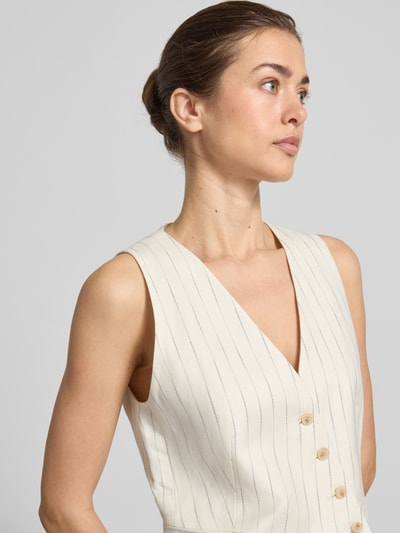 Frauenmodel trägt Weste aus Leinen-Mix mit asymmetrischem Schnitt und Nadelstreifen von Christian Berg Woman Selection, V-Ausschnitt, Knopfleiste, angedeutete Leistentaschen, cremefarben mit feinen Nadelstreifen, Leinen-Viskose-Anteil, Nahaufnahme Oberkörper.