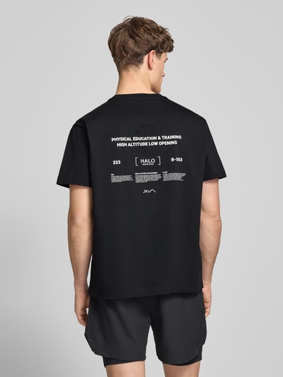 Männermodel trägt schwarzes T-Shirt mit weißem Label-Print von HALO, reine Baumwolle, Regular Fit, Rundhalsausschnitt, Ganzkörperansicht Rückansicht.