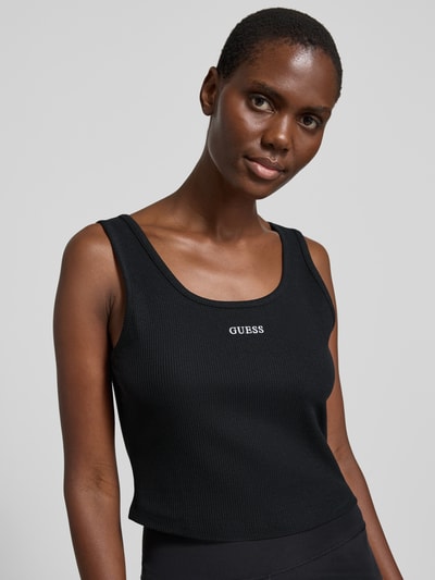 Frauenmodel trägt Slim Fit Top mit Logo-Stitching Modell 'Circe' von Guess in Schwarz, elastischer Baumwoll-Mix, Nahaufnahme Oberkörper.