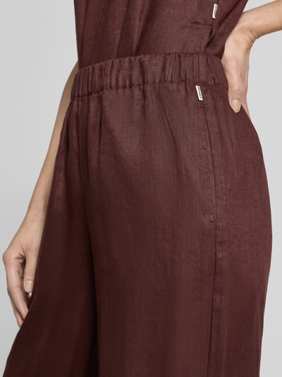 Kobieta nosi Wide Leg Leinenhose mit elastischem Bund Modell 'MOSSI' od ECOALF, czysty len, kolor ciemny brąz, szerokość w rozmiarze 36: 36 cm, długość wewnętrzna nogawki 79 cm, zbliżenie na biodra.