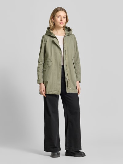 Kobiece modelka nosi parkę z bawełny khujo Parka mit Pattentaschen Modell 'NIKA', krój regular fit, kaptur, kieszenie z patką, długość tyłu w rozmiarze S 81 cm, szerokość ramion w rozmiarze S 40 cm, szerokość klatki piersiowej w rozmiarze S 51 cm, długość rękawów w rozmiarze S 60 cm, kolor oliwkowy, widok całej sylwetki od przodu.