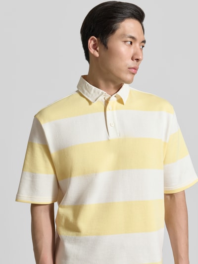 Männermodel trägt Relaxed Fit Poloshirt im Allover-Look von MCNEAL aus Baumwoll-Mix mit Knopfleiste, sanfte Gelb-Weiß-Töne, Nahaufnahme Oberkörper. Rückenlänge bei Größe M: 70 cm.