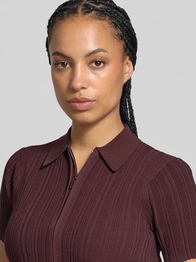 Frauenmodel trägt Shirt mit Zweiwege Reißverschluss von Victoria Beckham in Dunkelrot mit Rippstrickstruktur, Nahaufnahme Oberkörper.