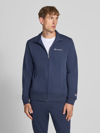 Mężczyzna nosi 'Sweatanzug mit Label-Details' od Champion w kolorze granatowym, Mieszanka bawełny, prosty krój, stójka, zamek błyskawiczny, detale z logo, wpuszczane kieszenie boczne, elastyczny pas, Szerokość w rozmiarze M: 76 cm, Długość tyłu w rozmiarze M: 70 cm, Szerokość ramion w rozmiarze M: 51 cm, Długość rękawów w rozmiarze M: 69 cm, Długość wewnętrzna nogawki w rozmiarze M: 76 cm, Ganzkörperansicht z przodu