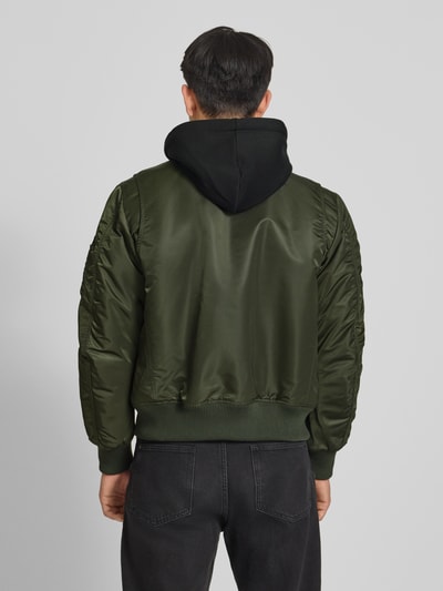 Männermodel trägt Bomberjacke mit Kapuze und Reißverschlusstaschen von Superdry in Olivgrün, Regular-Fit, Rückenansicht, Kontext: Herren Bomberjacke von Superdry, Kapuze, Reißverschluss, Reißverschlusstaschen, Rückenlänge 56 cm, Schulterbreite 45 cm, Brustweite 60 cm, Ärmellänge 68 cm. Ganzkörperansicht Rückansicht.