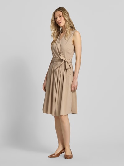 Frauenmodel trägt Kleid mit V-Ausschnitt in Wickel-Optik von More & More, Beige, Baumwoll-Mix, Tailliert, Ärmelloses-Design, Taillenband, Ganzkörperansicht von vorne.