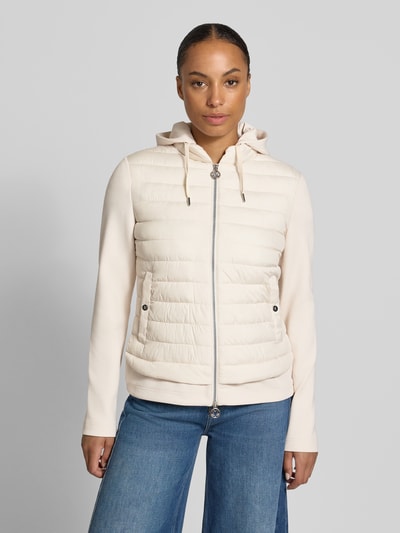 Modelka nosi kurtkę 'Jacke aus Baumwoll-Mix in Stepp-Optik' od FUCHS SCHMITT, mieszanka bawełny, krój taliowany, z efektem pikowania, kaptur z tunelem, zamek błyskawiczny dwustronny, Długość tyłu w rozmiarze 36: 59 cm, Szerokość ramion w rozmiarze 36: 40 cm, Szerokość klatki piersiowej w rozmiarze 36: 48 cm, Długość rękawów w rozmiarze 36: 67 cm, jasny beż, proste linie, gładkie i pikowane tekstury, widok całej sylwetki z przodu.