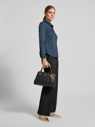 Vrouwenmodel draagt zwarte Handtasche in Leder-Optik Modell 'NOELLE' van GUESS met logodetail, hoofdvak met ritssluiting, schouderband, breedte 27 cm, lengte 24 cm, diepte 12 cm, schouderbandlengte 124 cm, kleuren zwart en goud, gladde textuur, volledige lichaamsvooraanzicht.