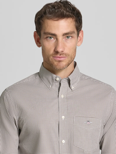 Männermodel trägt Regular Fit Freizeithemd aus reiner Baumwolle von GANT in braun kariert, klassische Knopfleiste, Nahaufnahme Oberkörper.