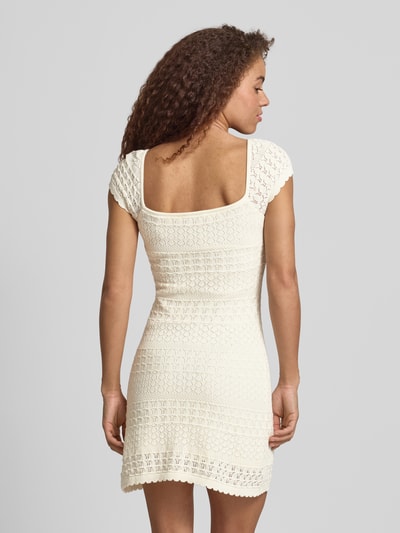 Frauenmodel trägt Strickkleid mit Strukturmuster und Wellensaum von REVIEW in Creme, reine Baumwolle, gerader Schnitt, Minikleid, Ganzkörperansicht Rückansicht.