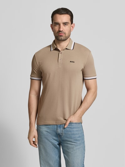Mężczyzna model nosi Regular Fit Poloshirt aus reiner Baumwolle Modell 'PADDY' od BOSS Green, jednolity beżowy, tkanina typu pique, krótki rękaw, nadruk z logo, kołnierzyk polo, zapięcie na trzy guziki. Ganzkörperansicht von vorne.