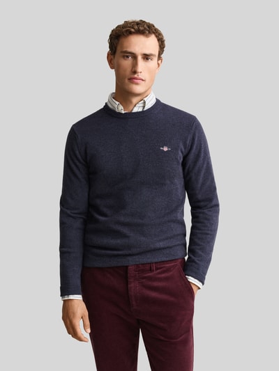 Männermodel trägt dunkelblauen Regular Fit Pullover aus reiner Wolle von GANT, dezente Struktur, kombiniert mit bordeauxfarbener Hose, Nahaufnahme Oberkörper.