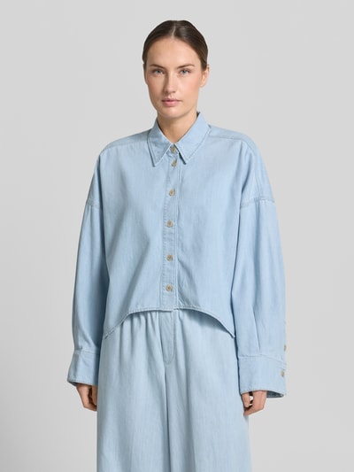 Frauenmodel trägt Relaxed-Fit Damen Hemdbluse in Denim-Optik Modell 'Oshia' von Drykorn aus Reine Baumwolle, Knopfleiste, Langärmelig, Hemdblusenkragen, hellblaue Farbe, glatte Textur, Rückenlänge 55 cm, Ärmellänge 47 cm, Ganzkörperansicht von vorne.