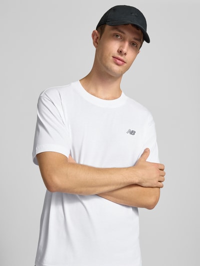Männermodel trägt weißes T-Shirt mit Label-Stitching Modell 'ESSENTIALS' von New Balance, reine Baumwolle, Nahaufnahme Oberkörper.