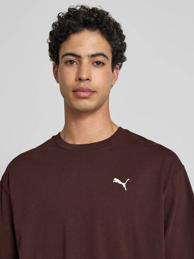 Männermodel trägt T-shirt mit ronde hals van PUMA PERFORMANCE in bruin, puur katoen, relaxed fit, logoprint, nahaufnahme oberkörper.
