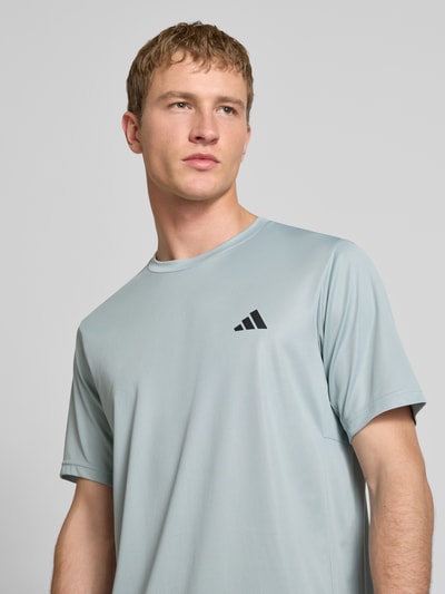 Männermodel trägt T-Shirt mit Logo und Rundhalsausschnitt von adidas Training in Hellgrau, glatte Textur, Regular Fit, Nahaufnahme Oberkörper.
