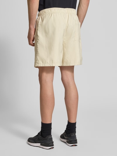 Männermodel trägt Shorts mit Label-Stitching und elastischem Bund von Nike in Beige, Regular-Fit, Tunnelzug, Rückansicht Ganzkörperansicht. Bundweite bei Größe M: 41 cm, Innenbeinlänge: 14 cm.