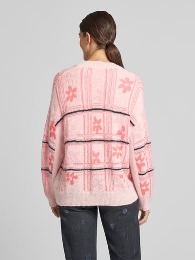 Frauenmodel trägt Oversized Cardigan mit Alpaka-Mohair-Anteil von Marc Cain in Rosa mit floralem Muster, Rückenansicht, Material-Mix.