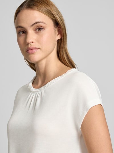 Frauenmodel trägt T-Shirt mit Rundhalsausschnitt und Zierperlen von More & More aus Micromodal-Mix, glatte Struktur, Nahaufnahme Oberkörper.