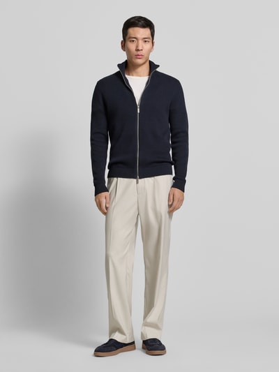Männermodel trägt Regular Fit Strickjacke aus reiner Baumwolle Modell 'DAME' von SELECTED HOMME in Dunkelblau, Zweiwege-Reißverschluss, unifarben, Stehkragen, gerippte Abschlüsse, Ganzkörperansicht von vorne