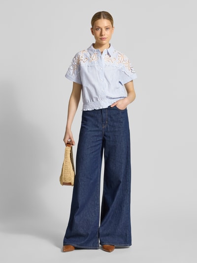 Frauenmodel trägt Regular Fit Hemdbluse mit Häkelspitze Modell 'LOlITA' von SUNCOO PARIS aus Reine Baumwolle, hellblau mit weißem Muster, Kentkragen, 1/2-Arm, Raffung, kombiniert mit weiter Jeans, Ganzkörperansicht von vorne.