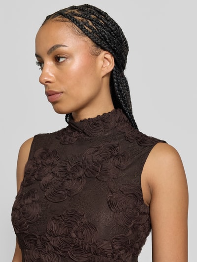 Frauenmodel trägt Maxikleid mit floralem Allover-Besatz von ROTATE, brauner Spitzenstoff, ärmelloses Design, Nahaufnahme Oberkörper.