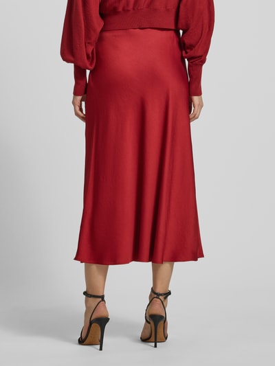 Vrouwenmodel draagt Midirock in A-lijn model 'URA' van Drykorn in rood, materiaal-mix met stretch, volledige lengte, achteraanzicht.